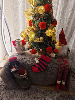 Decorated Christmas tree with gold and red ornaments, Santa figure, striped stockings and elf legs on gray fur