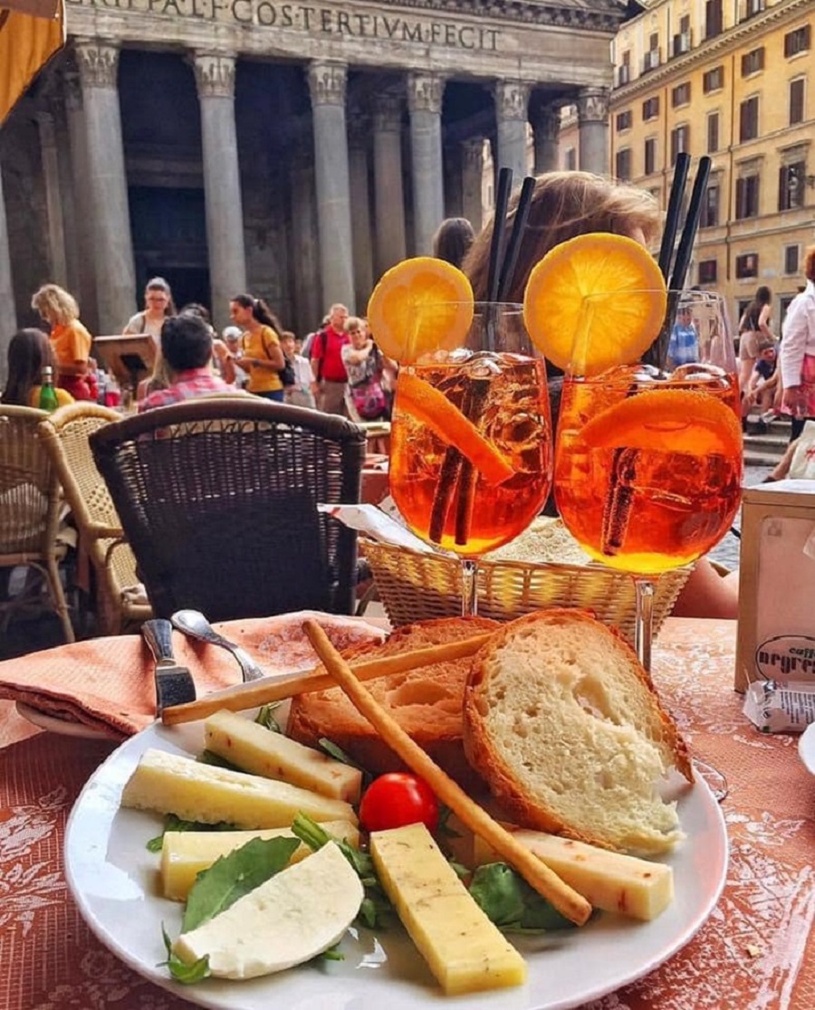 Orange Aperol Spritz drinks with appetizer plate at outdoor café in Rome with Pantheon in background