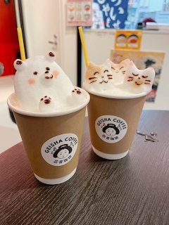 Two coffee cups with 3D latte foam art shaped like a bear and cats on a table