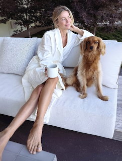 Woman in white robe relaxing on patio couch with brown dog and coffee