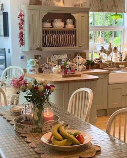 Cozy country kitchen with green cabinets, plate rack, flowers, fruit bowl, and lit candle on dining table