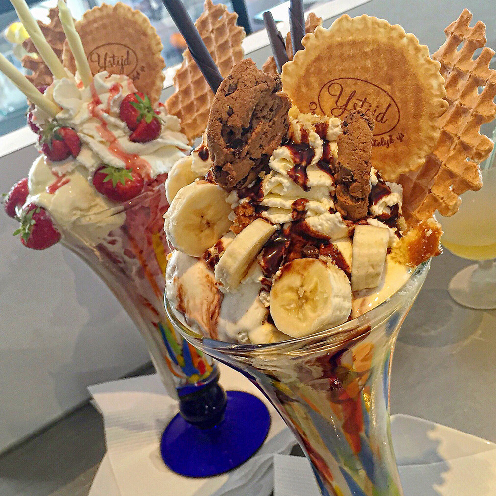 Tall glass filled with ice cream, fruit, waffle cookies, whipped cream and chocolate sauce