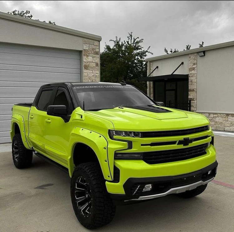 Bright lime green lifted pickup truck parked on concrete outside industrial buildings