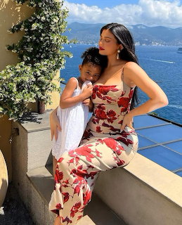 Woman in red floral dress sitting with small child on terrace with ocean view