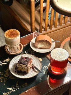 Overhead view of café table with cappuccino, tea, tiramisu slice, and Swiss roll cake on plates