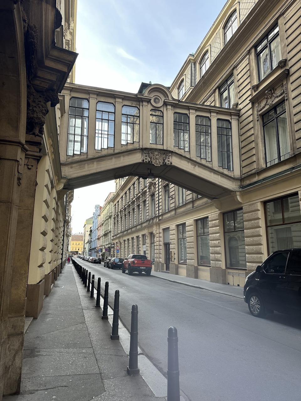 Ornate covered bridge linking two historic buildings over a quiet city street in Prague