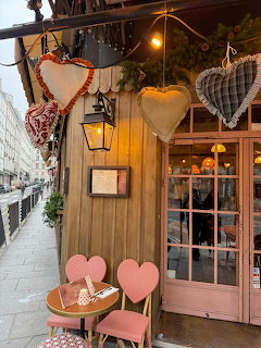 Wooden Paris cafe entrance with heart decorations, pink chairs, and a narrow sidewalk
