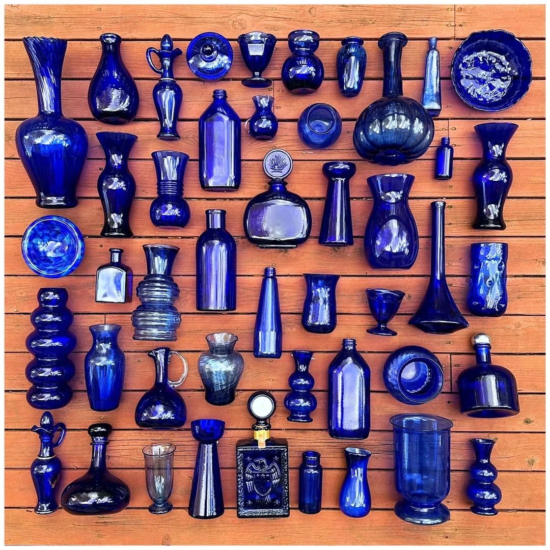 Cobalt blue glass bottles, vases, and dishes arranged on a wooden surface