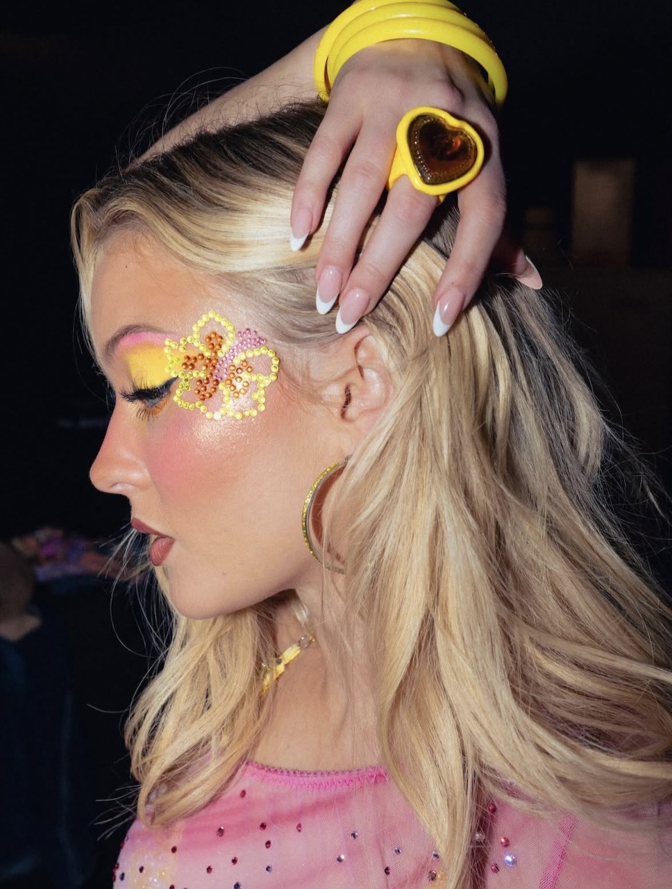 Blonde woman with yellow and pink glitter floral eye makeup and yellow heart hair clip