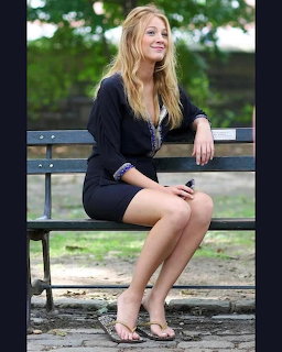 Woman with long blonde hair sitting on park bench wearing black cardigan and skirt