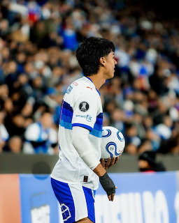 Soccer player in white jersey with blue accents holding a ball at stadium