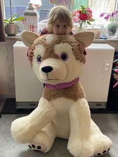 Young child peeking over a large stuffed dog toy indoors near a window
