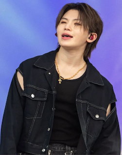 K-pop idol in black denim jacket with gold cross necklace performing on stage with blue background