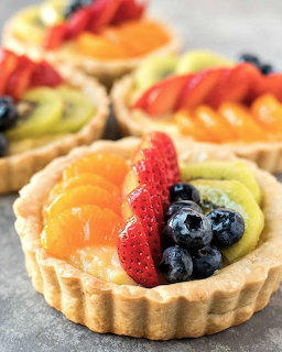 Several fruit tartlets with custard filling topped with fresh strawberries, kiwi, oranges, and blueberries