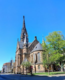Gothic church with tall pointed spire and arched windows against a bright blue sky in Dresden