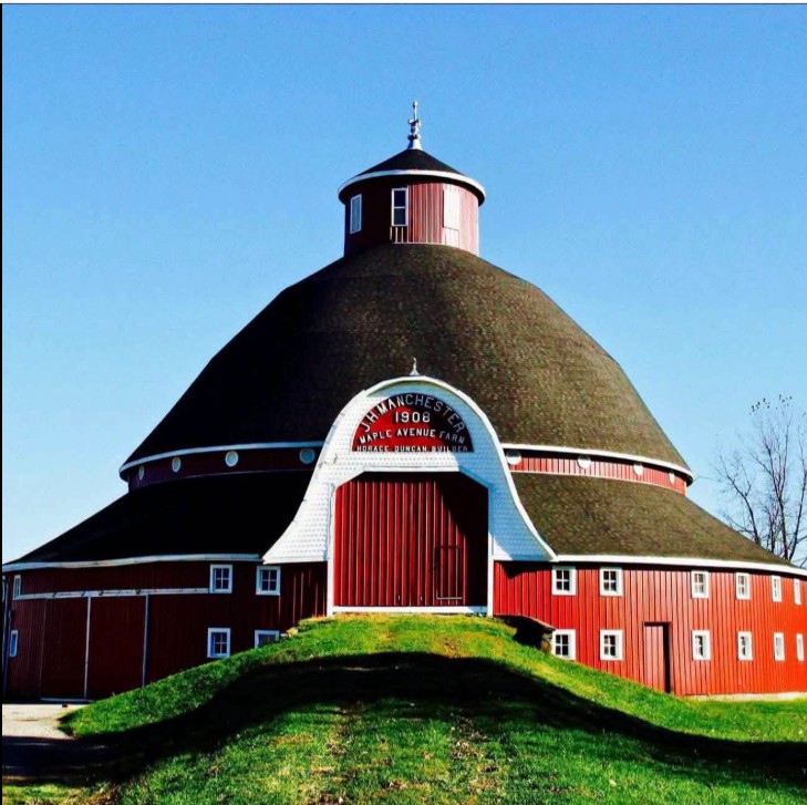 Red round barn with a domed roof on a grassy hill beneath a clear blue sky