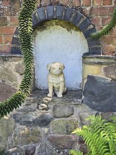 Stone dog statue in white-painted brick archway with ferns