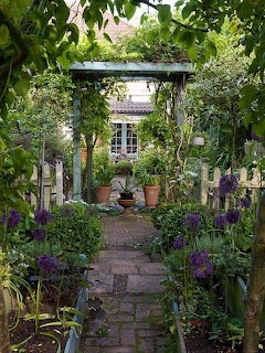 Stone garden path beneath a wooden archway surrounded by lush green plants and purple flowers