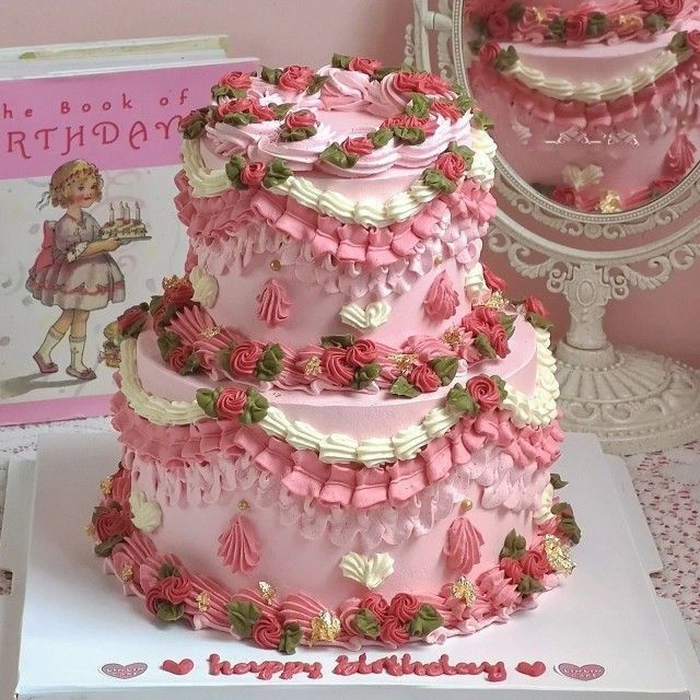 Three-tier pink frosted cake decorated with fresh strawberries, cream rosettes, and vintage ornaments on white pedestal stand