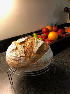 Round rustic bread loaf on a cooling rack on a dark counter with fruit behind it