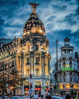 Ornate Metropolis building with dome and statue illuminated at dusk in Madrid cityscape