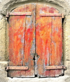 Old wooden shutters with peeling orange paint and metal hinges on weathered stone wall