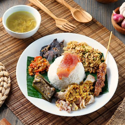 Balinese roast pork rice plate with sides, soup, and wooden spoon on woven bamboo placemat