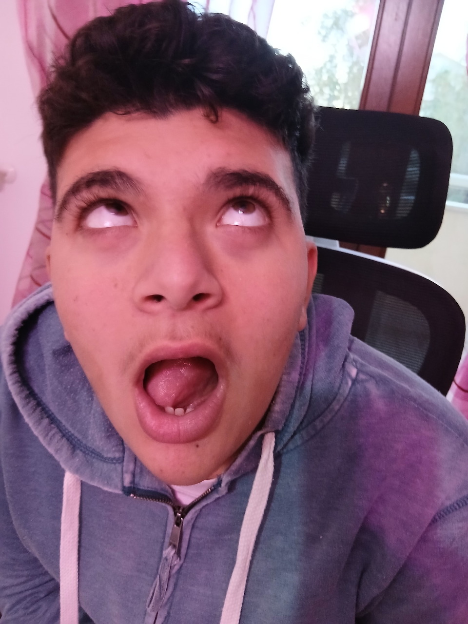 Young man with mouth wide open and eyes rolled back making a silly face, wearing a grey hoodie