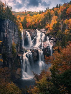 Large multi-tiered waterfall cascading down rocky cliffs surrounded by colorful autumn trees