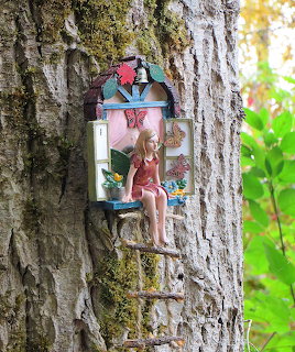 Miniature fairy house door with a small seated fairy figure mounted on a tree trunk