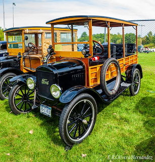 Black 1924 Ford Model T woody wagon with wood body panels and green spoked wheels on grass at car show