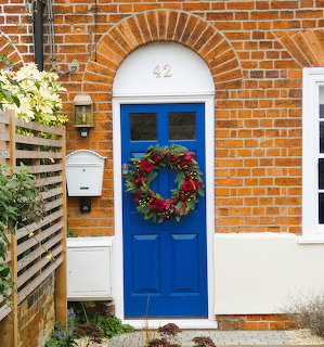 Blue front door with colorful flower wreath on orange brick house, white arch above showing number 42