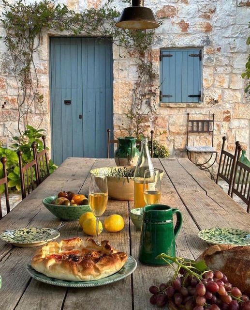 Outdoor breakfast table with pastries, fruit, and drinks on rustic stone patio with blue wooden doors