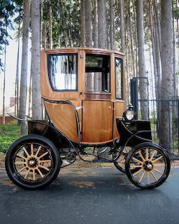 Early 1900s Woods Electric automobile with wooden enclosed cabin and spoke wheels in forest setting