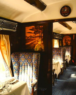 Elegant vintage train interior with ornate wood panels, armchairs, decorative curtains, and luxury corridor