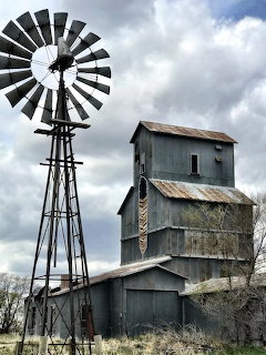Old grain elevator building with windmill under stormy sky