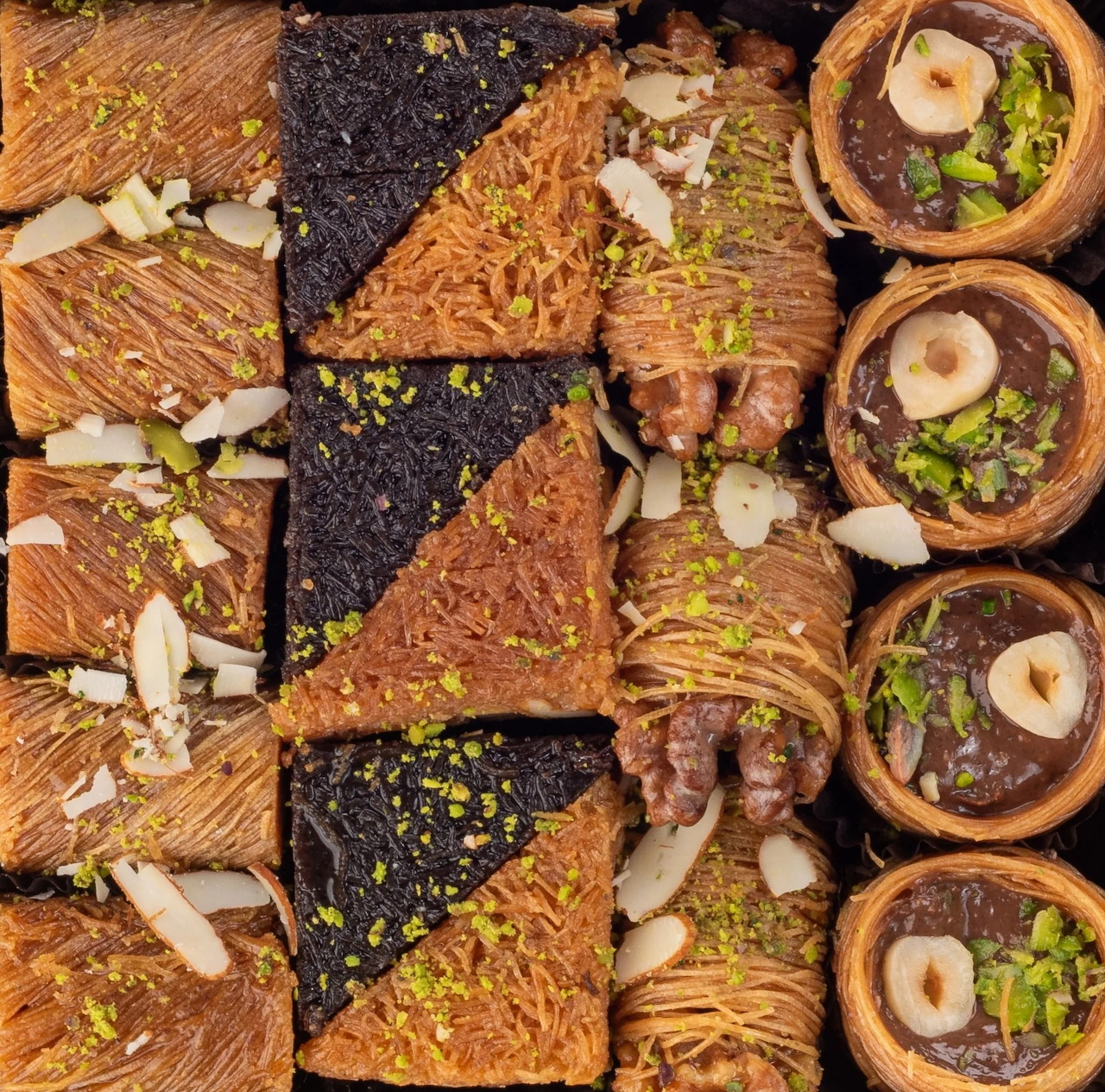 Top view of assorted kunafa pastries with pistachios, almonds, and cream in a box