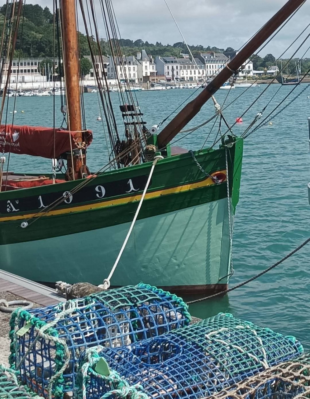Green fishing boat with rigging moored at harbor dock with blue lobster traps and coastal town behind