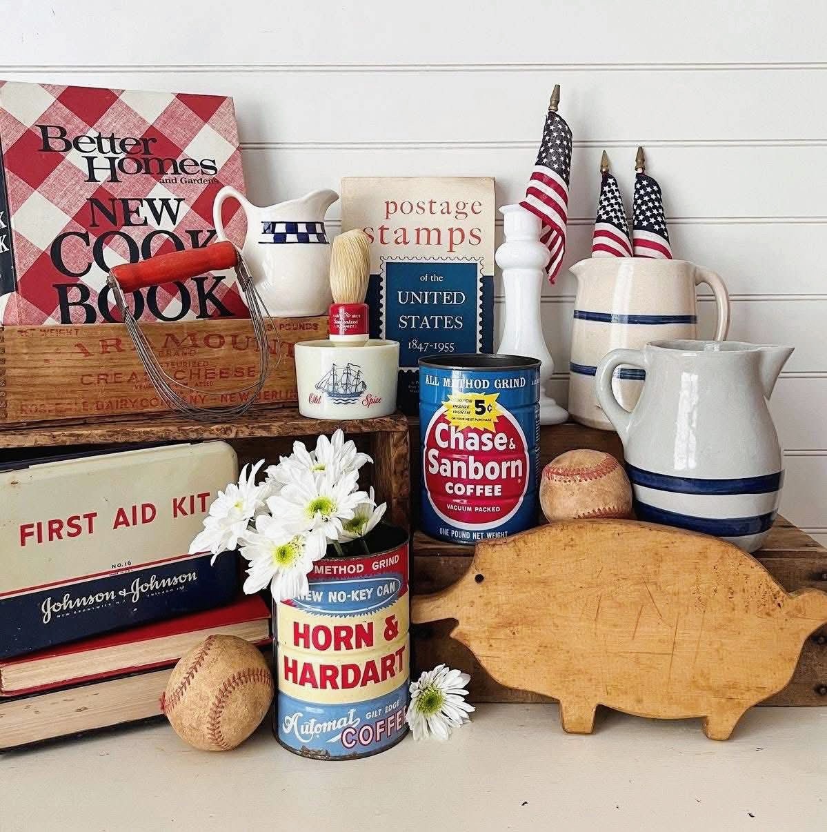 Vintage kitchen decor arrangement with antique tins, books, flags, and ceramic pitchers on white wood background