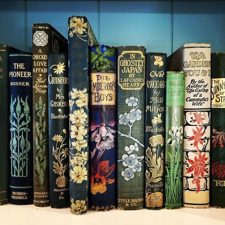Row of vintage books with ornate floral spine designs in blue, green, and gold on a shelf