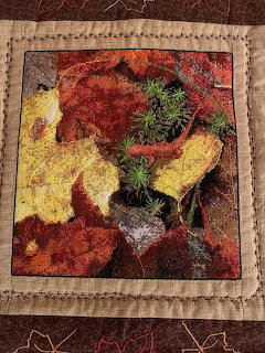 Cross stitch textile art of autumn leaves in red, yellow, and gold with tan fabric border and handstitching