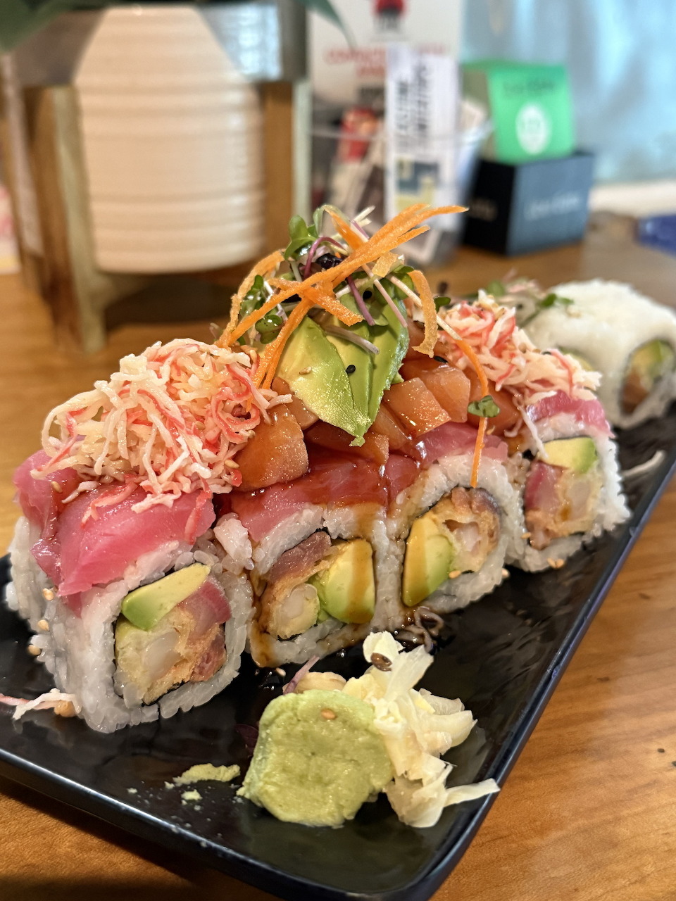 Colorful sushi roll topped with tuna, avocado, shredded carrots and greens on a black plate