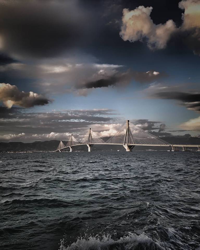 Cable-stayed bridge with tall white pylons crossing water under dramatic stormy clouds