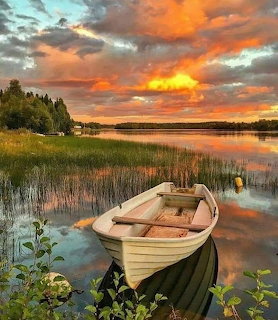 Wooden rowboat on a calm lake shore with colorful sunset clouds reflected in the water