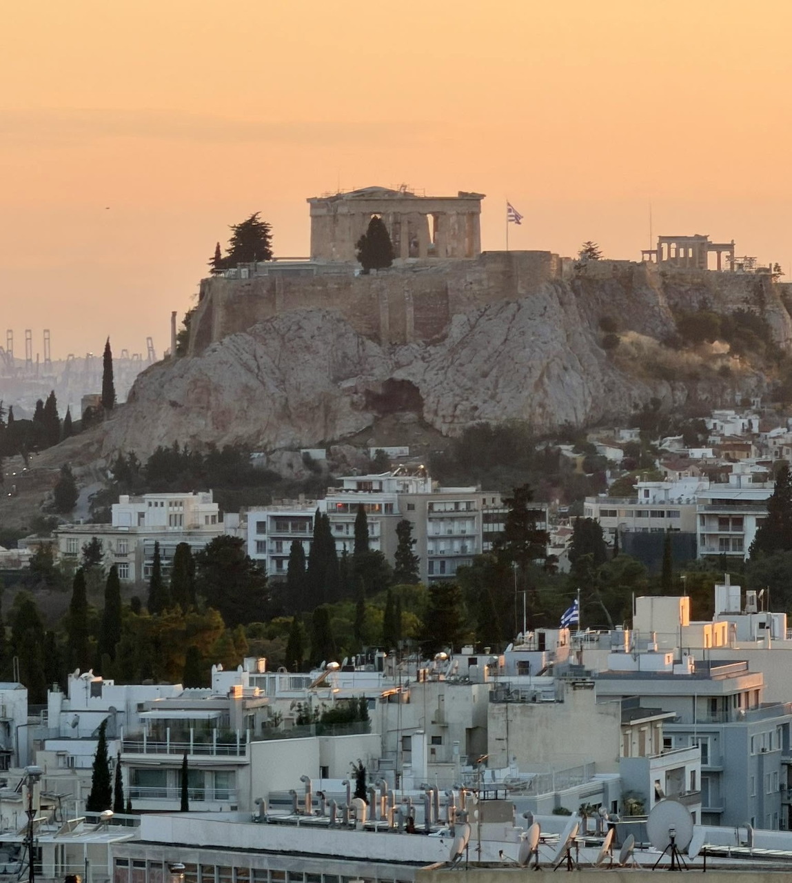 The Acropolis and Parthenon overlooking Athens rooftops at sunset with an orange sky