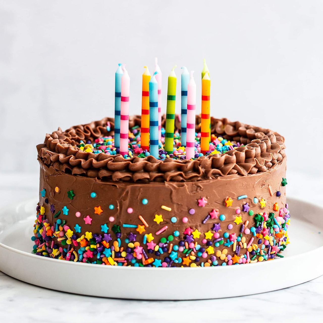 Chocolate birthday cake with colorful sprinkles and striped candles on a white plate