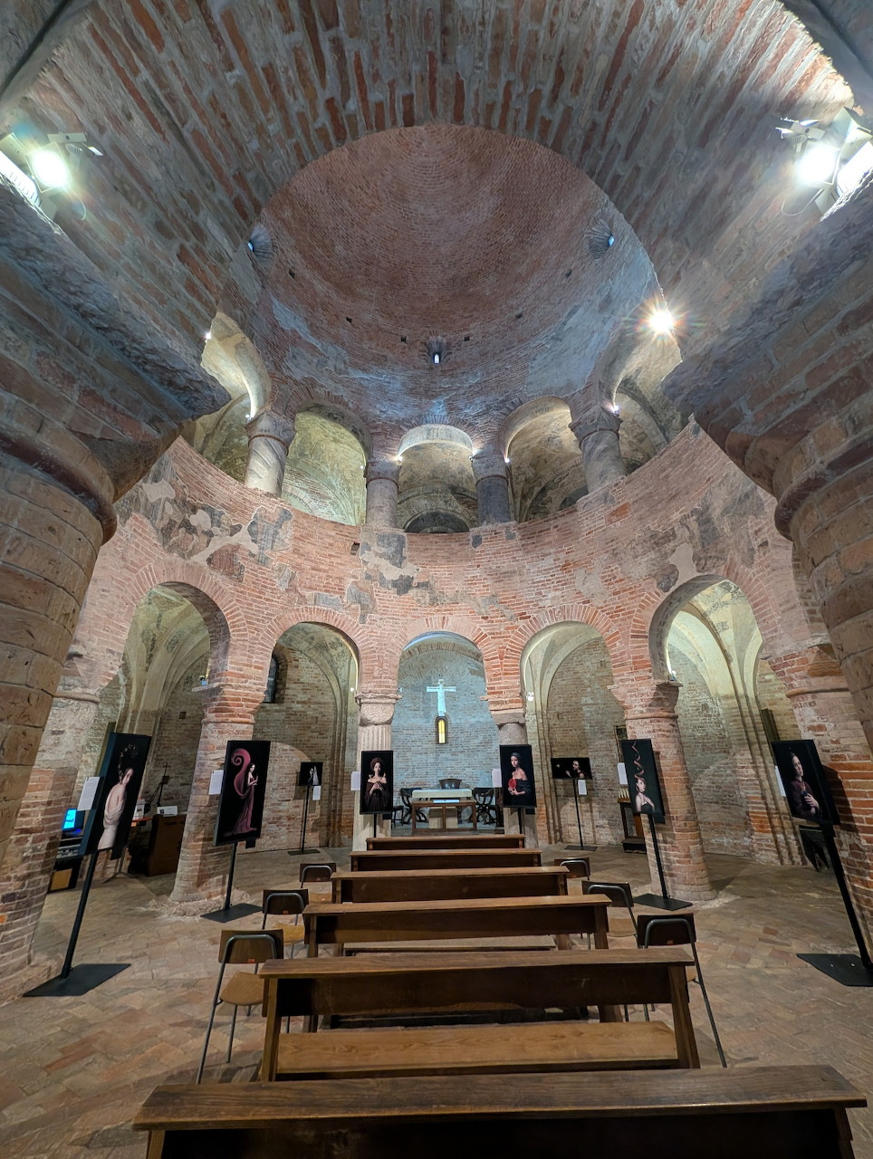 Interior of Rotonda di San Lorenzo with circular brick dome, columns, arches, wooden benches and altar in Mantova
