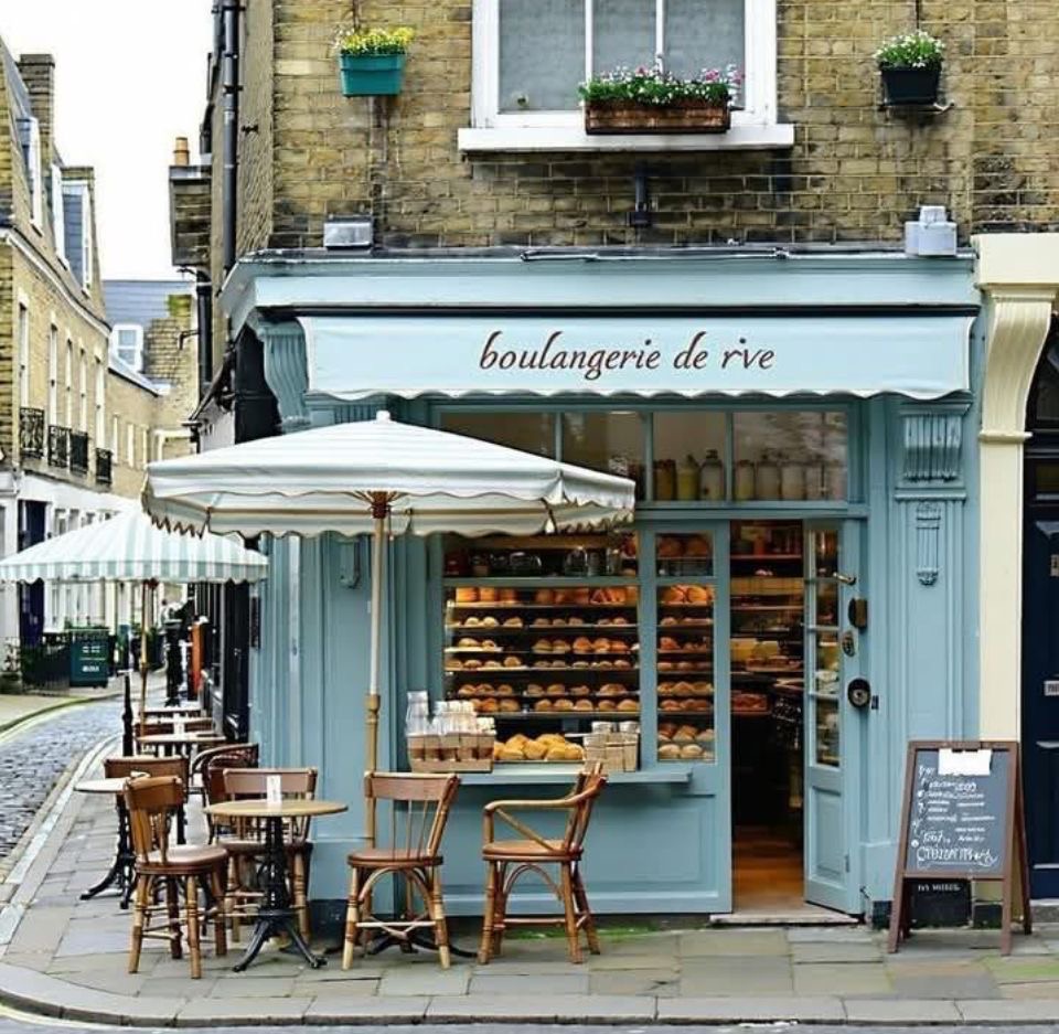 Pastel blue bakery storefront with outdoor tables and bread display on a narrow street
