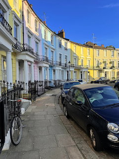 Pastel terrace houses on a curved London street with parked cars and a bicycle under a blue sky