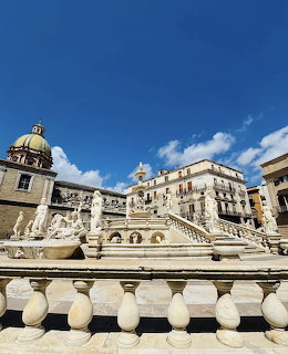 Baroque marble fountain with statues and steps in a Sicilian city square with historic buildings